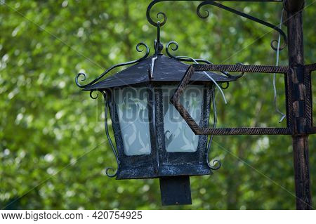 Vintage Lantern On A Pole In The Park Against A Background Of Green Foliage