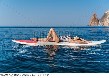 Sporty Girl On A Glanders Surfboard In The Sea On A Sunny Summer Day. In A Striped Swimsuit, He Lies