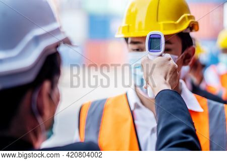 Female Foreman Wearing A Mask Measures The Temperature For A Worker In A Safety Suit. They Stood And