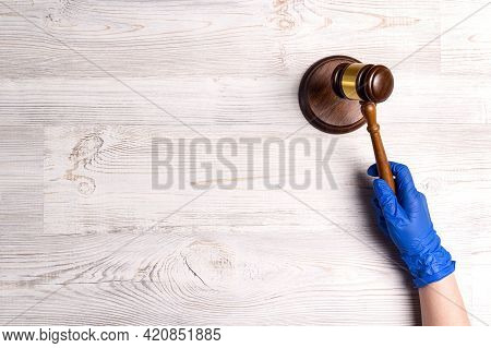 Hand Of A Judge In A Medical Glove Holds A Gavel. Judicial System And Law During The Coronavirus.