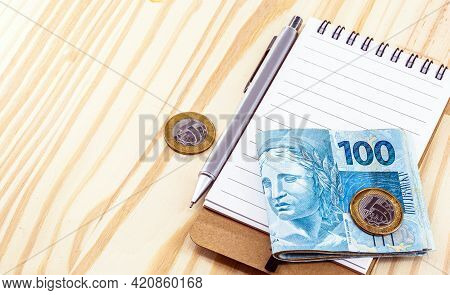Banknotes And Coins Of Brazil Money, On Table With Notepad And Pen