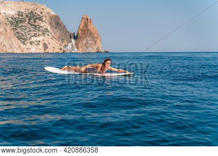 Sporty Girl On A Glanders Surfboard In The Sea On A Sunny Summer Day. In A Striped Swimsuit, Lying O