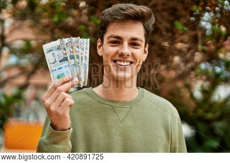 Young hispanic man smiling happy holding peruvian soles banknotes at the city.