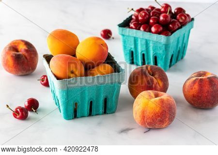 Cardboard Containers Of Apricots And Cherries With Peaches Surrounding.