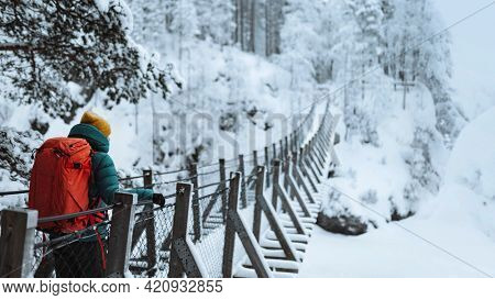 Woman crossing a suspension bridge in a snowy forest, Finland