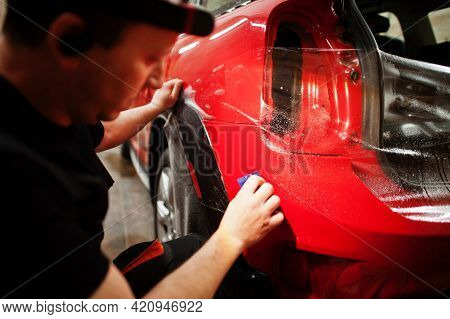 Car Service Worker Put Anti Gravel Film On A Red Car Body At The Detailing Vehicle Workshop. Car Pro