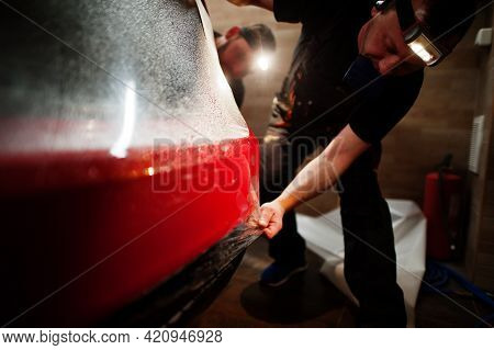 Car Service Worker Put Anti Gravel Film On A Red Car Body At The Detailing Vehicle Workshop. Car Pro