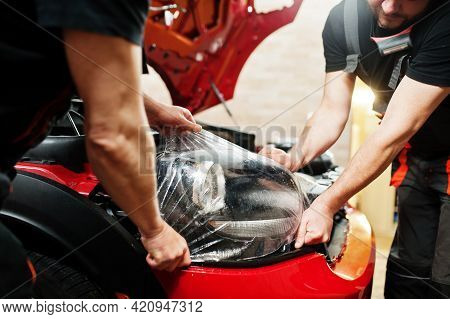 Car Service Worker Put Anti Gravel Film On A Red Car Body At The Detailing Vehicle Workshop. Car Pro