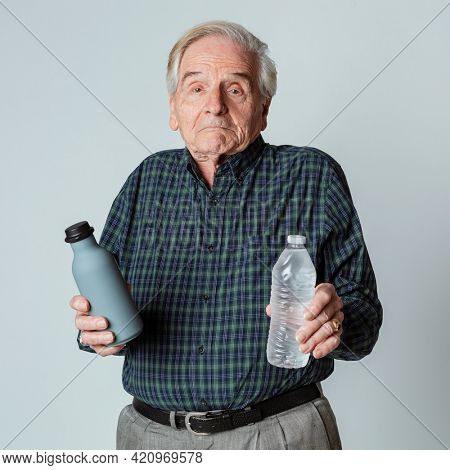 Puzzled senior man holding a reusable and a plastic water bottle