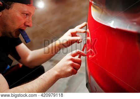 Car Service Worker Put Anti Gravel Film On A Red Car Body At The Detailing Vehicle Workshop. Car Pro