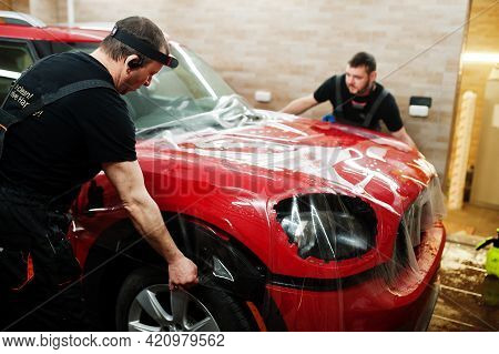 Car Service Worker Put Anti Gravel Film On A Red Car Body At The Detailing Vehicle Workshop. Car Pro