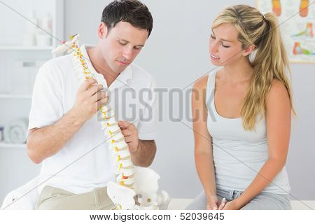 Handsome physiotherapist showing patient something on skeleton model in bright office