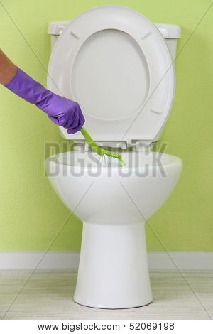 Woman hand with brush cleaning a toilet bowl in a bathroom
