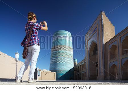 Young lady taking a picture of oriental buildings in Itchan Kala ancient town. Khiva, Uzbekistan