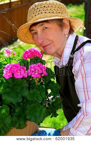 Senior woman with a pot of geranuim flowers in her garden