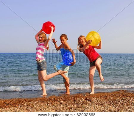 Three girls on a sandy beach being silly with colorful balls