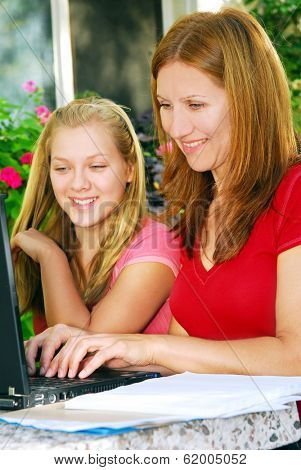 Mother and daughter working on computer at home in the backyard