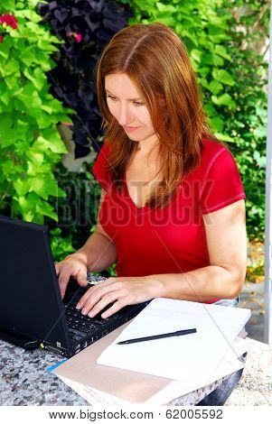 Mature woman working on portable computer in her garden at home