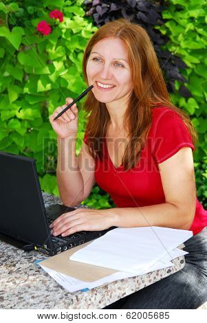 Happy mature woman working on a portable computer in her garden