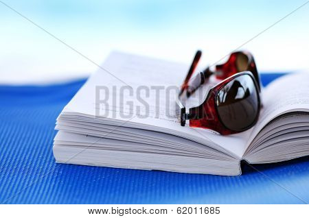 Sunglasses and open book on beach chair - summer vacation concept