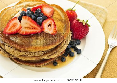 Stack of buckwheat pancakes with fresh berries and maple syrup