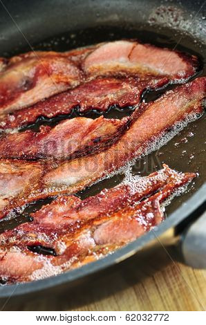 Bacon strips sizzling on a frying pan