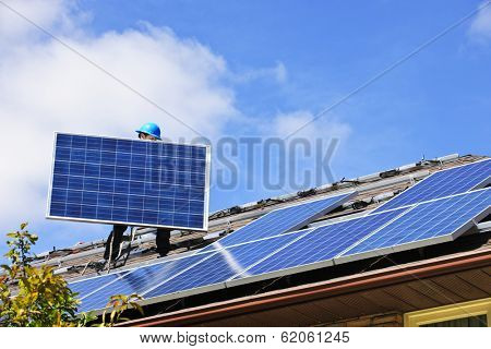 Worker installing alternative energy photovoltaic solar panels on roof
