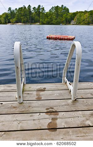 Wet footprints on dock with ladder and diving platform at lake in Ontario Canada