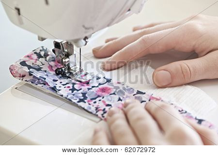 Closeup of hands guiding fabric through sewing machine needle and thread