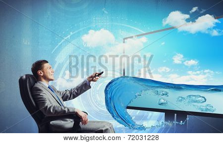 Young businessman sitting in chair behind tv with click in hand