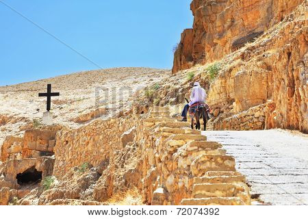 On the road, paved with stone, climbs on a donkey pilgrim in white clothes. Wadi Kelt, the road to the monastery of St. George