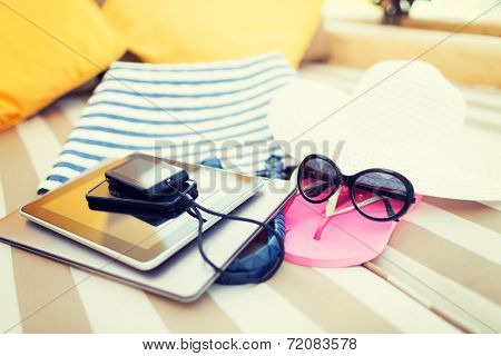 beach, summer vacation and technology concept - close up of tablet pc, notebook, smartphone and summer accessories on beach