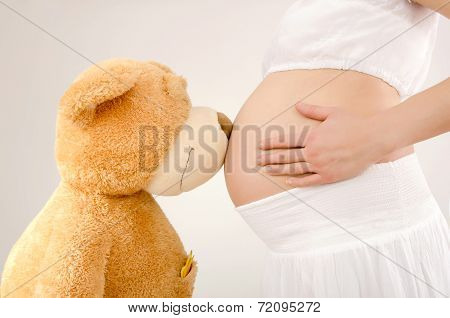 Close up on pregnant belly and a big teddy bear.