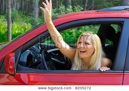 Piękna kobieta kierowca w czerwony samochód błyszczący na zewnątrz uśmiecha się i macha ręką