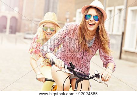 A picture of two girl friends riding a tandem bicycle in the city