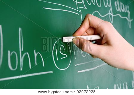 Teacher hand writing grammar sentences on blackboard background