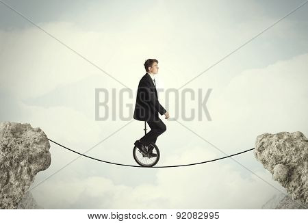 Brave business man riding an mono cycle between cliffs concept