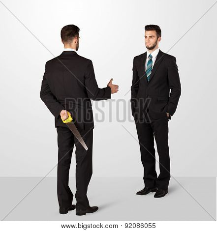 Two opposing businessman shake hands, one of them hiding a weapon behind his back