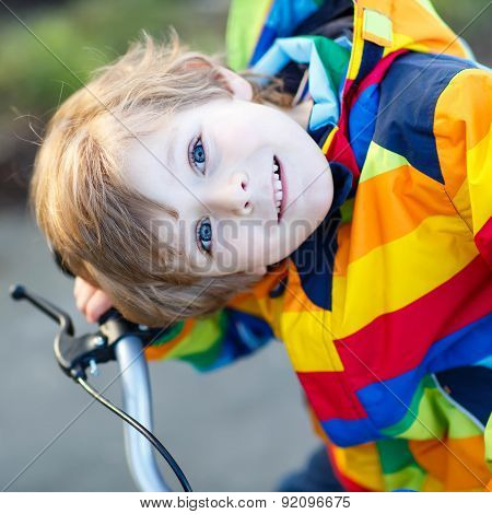 Kid Boy In Safety Helmet And Colorful Raincoat Riding Bike, Outdoors.