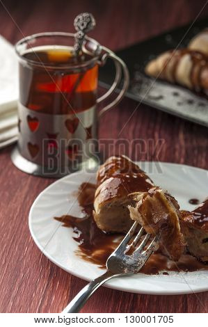 Fresh cut puff with banana and chocolate glaze on plate with fork and cup of tea on red wooden background. Selective focus.