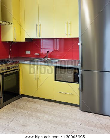 yellow kitchen with cupboards with hinged doors topped with a grey worktops and fitted with appliances including refrigerator microwave oven extractor hood a wall with a red tile and floor with soft sand grey laminate