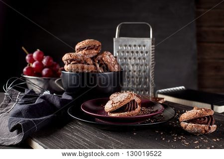 Italian maroni cookies on the plate and bowl with grapes cloth notebook on dark old wooden background