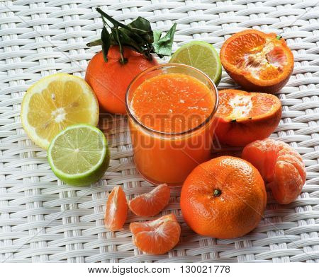 Glass of Freshly Squeezed Mixed Citrus Juice with Tangerines Limes Oranges and Lemons closeup on Wicker background