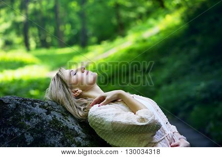 beautiful young girl resting in a forest on the rock