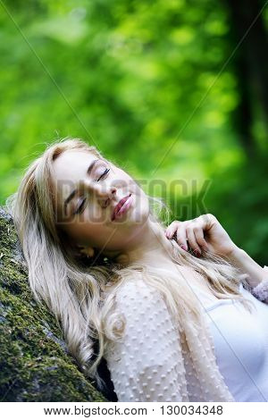 beautiful young girl resting in a forest on the rock