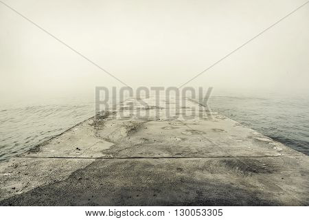 Stone pier in thick fog mystic. Toned image.