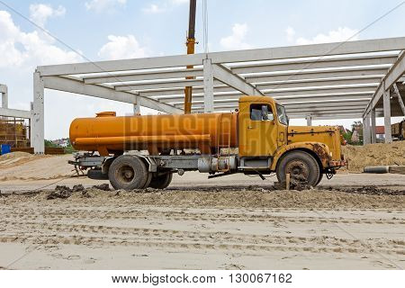 Yellow vintage tank truck is parked on building site. Landscape transform into urban area.