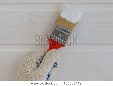 hand with brush in white paint near the wall