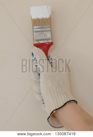 hand with brush in white paint near the wall