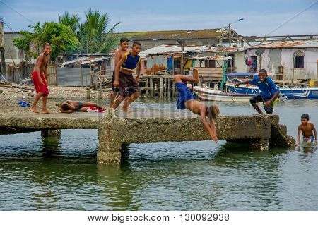 Muisne, Ecuador - March 16, 2016: Local kids and teenagers playing happily jumping from pier into ocean, posing for camera laughing, beautiful blue sky.